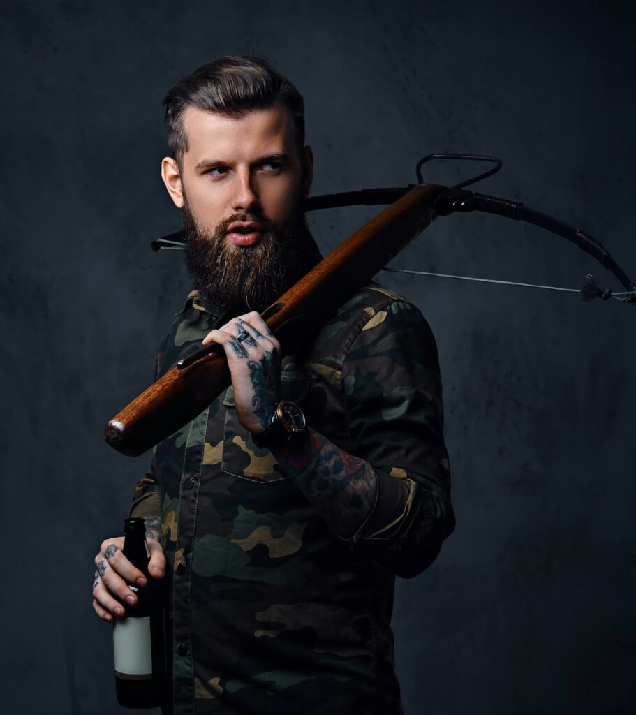 A man holds the craft beer bottle and a crossbow.