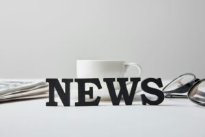 selective focus of news lettering near cup of coffee, glasses and newspaper on white